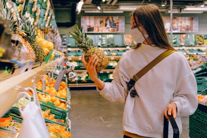 Woman Wearing Mask in Supermarket and holding a pineapple